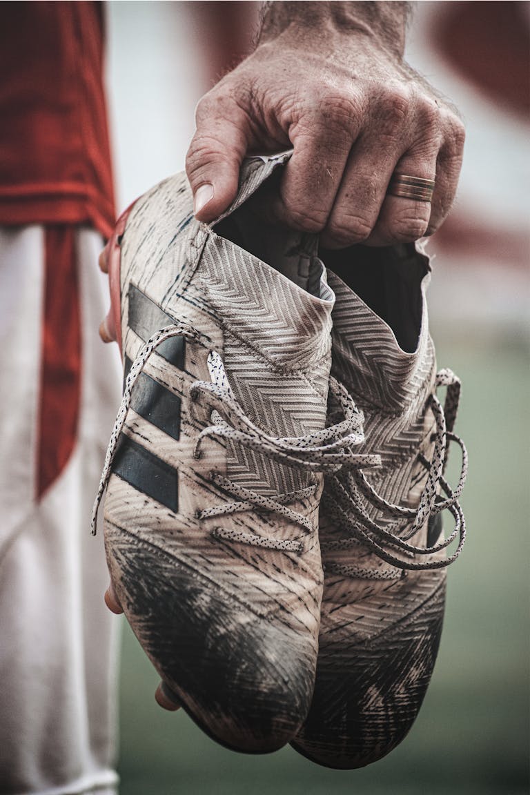 Detailed shot of a hand holding worn soccer cleats highlighting the sport's rugged nature.